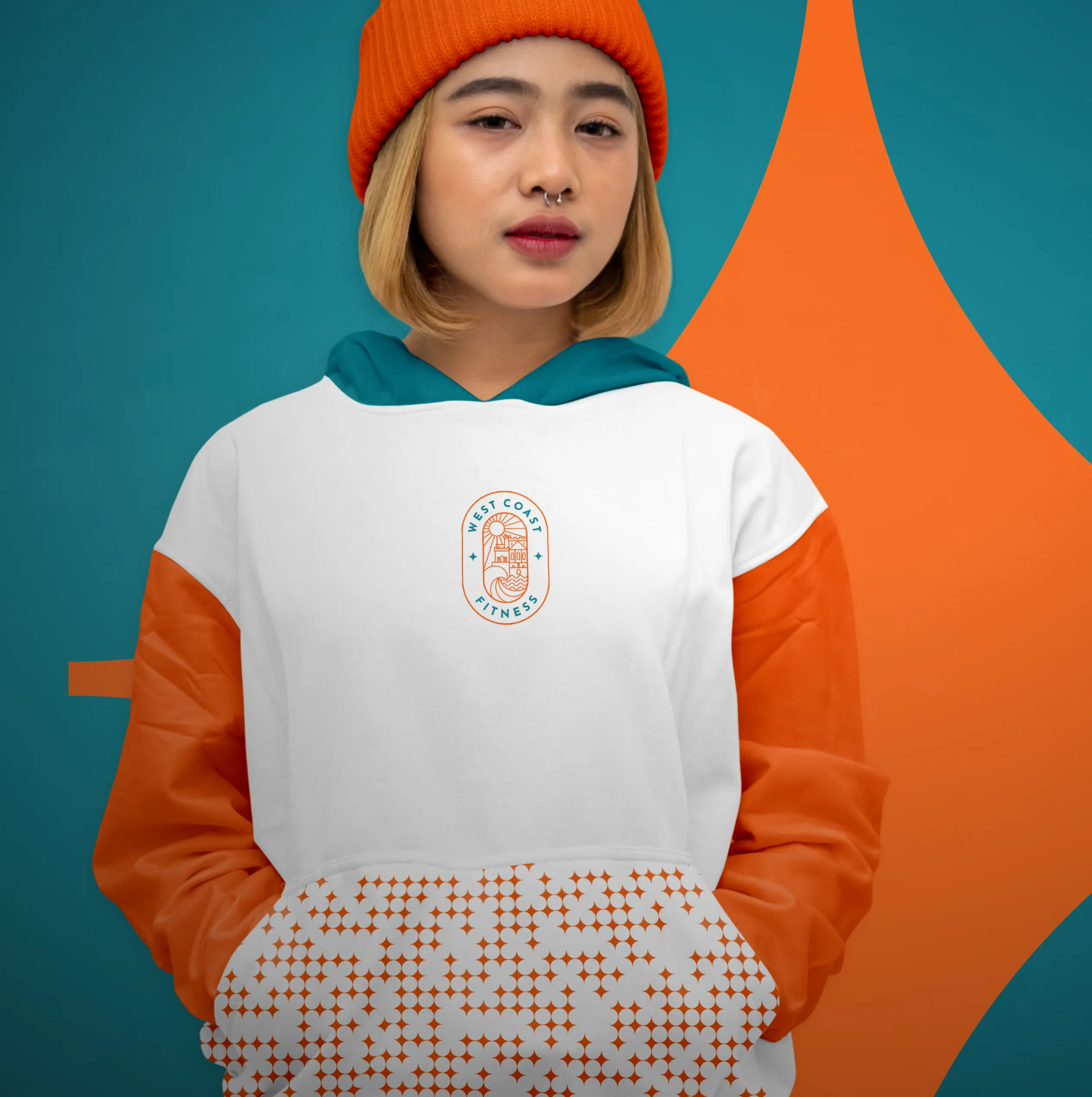 Young woman wearing a white hoodie with small West Coast Fitness logo on the chest, styled with an orange jacket and beanie against a teal and orange background